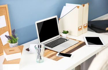 Fototapeta na wymiar Workplace with different devices, stationery and table on blue wall background