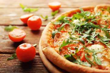 Margherita pizza with tomatoes and arugula on wooden background