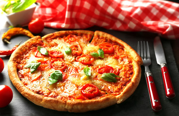 Margherita pizza with utensils and vegetable on slate plate