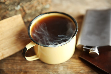 Metal mug of coffee with flask on wooden background