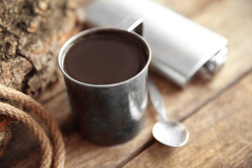 Metal mug of coffee with flask, spoon and rope on wooden background