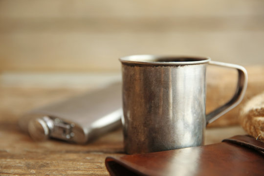 Metal mug of coffee with flask and rope on wooden background
