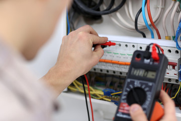 Young electrician measuring voltage in fuse board