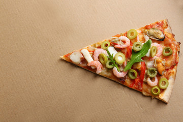 Pizza slice with seafood, red pepper and green olives on cardboard background
