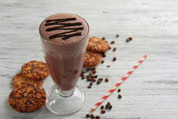 Glass of chocolate milkshake with cookies and coffee beans on wooden background