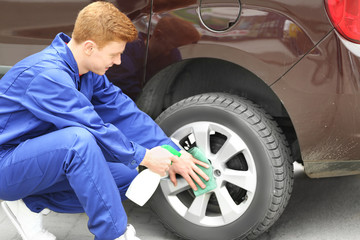 Young man with liquid detergent cleaning car wheel