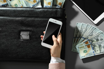 Businesswoman holding cellphone and brief case with money
