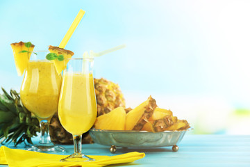 Pineapple smoothie in cocktail glasses with slices on blue blurred background