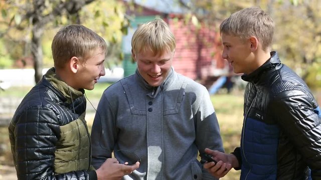 Friendly meeting of three young friends in autumn park. Two of the boys twin brothers.