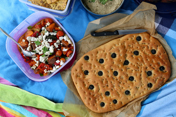 Top view of various picnic food: vegetable and feta salad and mediterranean olive bread.
