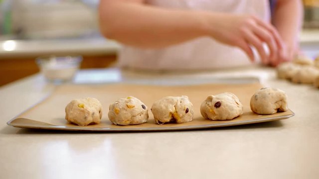 Chef places first row of hot cross bun dough balls on baking sheet in preparation for baking.  Slow motion, originally recorded in 4K at 60fps.