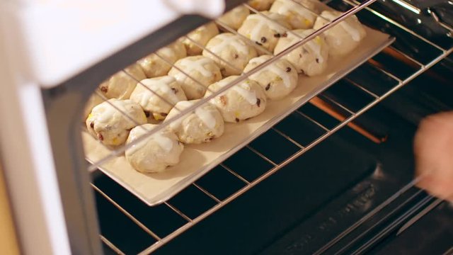 Pastry chef puts hot cross buns into an oven on a stainless steel baking tray.  Originally recorded in 4K and cropped.