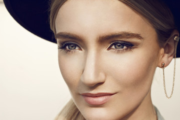 Fototapeta premium Close up of beautiful young blonde woman with black hat. Wearing denim vest. Her hair is tied to ponytail. 
