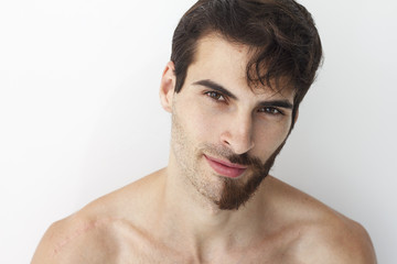 Man without a shirt, standing in front of a camera on a white background with half of his face with scruffy beard and messy hair, the other half has trimmed beards.