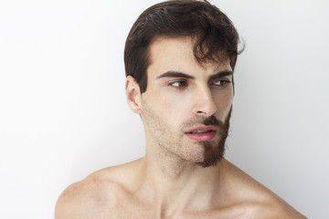 Man without a shirt, standing in front of a camera on a white background with half of his face with scruffy beard and messy hair, the other half has trimmed beards.