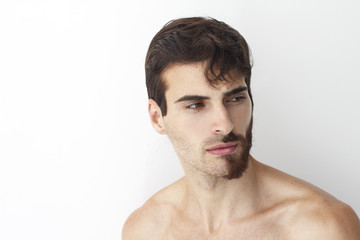 Obraz premium Man without a shirt, standing in front of a camera on a white background with half of his face with scruffy beard and messy hair, the other half has trimmed beards.
