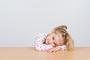  little girl resting head on wooden surface at table.