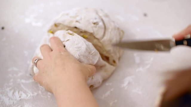 Chef cuts and shapes dough on floured kitchen work surface after letting it rise to make hot cross buns.  Originally recorded in 4K.