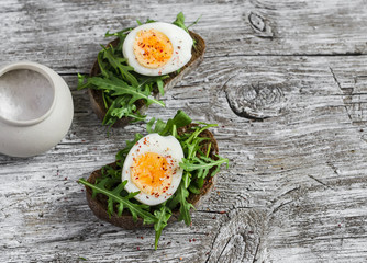 Sandwich with arugula and boiled egg on a wooden board. Healthy breakfast or snack