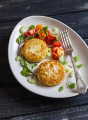 Potato cutlet and fresh tomato and celery salad on a light ceramic plate on dark wooden background.