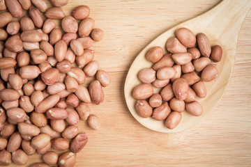 scoop of peanut and a pile of peanut on a wooden background