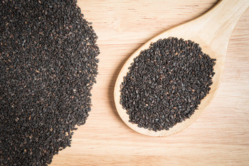 scoop of black sesame and a pile of black sesame on a wooden bac