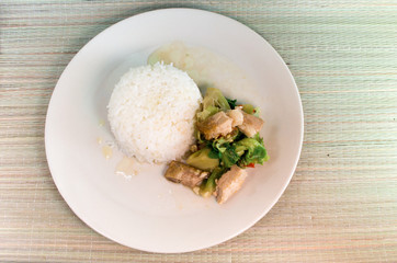 Thai food, Brussel sprout fried oyster dish with crispy pork with rice on a white plate, with woven wood background.