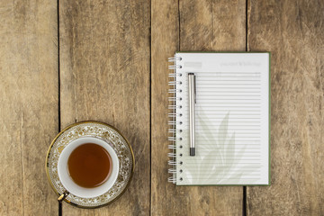 Notebook and a glass of tea or coffee on a wooden table.