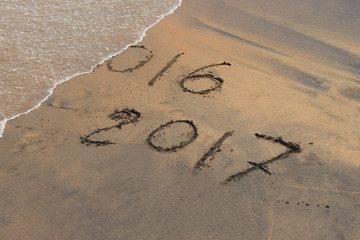 New Year 2017 is coming. New Year 2017 is coming concept - inscription 2016 and 2017 on a beach sand, the wave is covering digits 2016.
