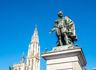 Fototapeta na wymiar Statue of Peter Paul Rubens with Cathedral of Our Lady in Background in Antwerp, Belgium, under clear blue sky. The cathedral is the highest church in the Benelux with 123 m (404 ft) of height.
