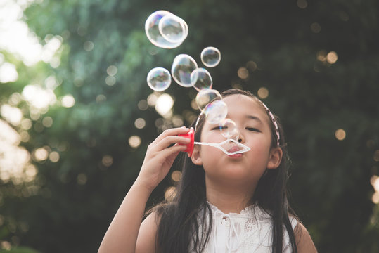 Cute asian girl is blowing a soap bubble