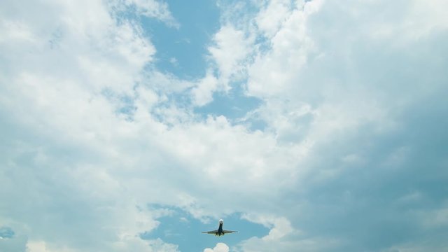Tilting Up to Commercial Passenger Airliner during Vertical Overhead Flyover on a Sunny Day with White Clouds in front of a Blue Sky