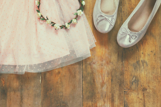 vintage chiffon girl's dress, floral tiara next to ballet shoes on wooden background. vintage filtered image
