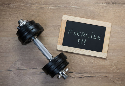 Concept for exercise and sport. Dumbbell and a message on a chalkboard on a wooden background