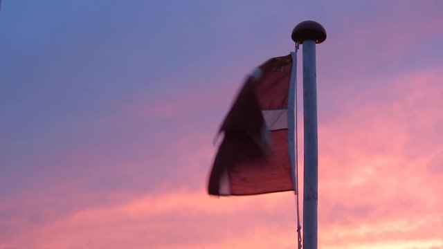 Danish Flag called Dannebrog at Sunset. Flag of Denmark Waving in the Wind in front of a purple yellow cloudy sky.