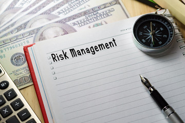 Conceptual image.Calculator, hundred dollar bills, pen, notebook and compass on wooden table with RISK MANAGEMENT words.