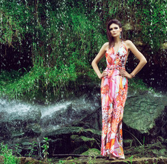Young woman in a fashion dress posing next to a waterafll