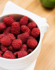 Raspberry in white plate on wooden table, closeup