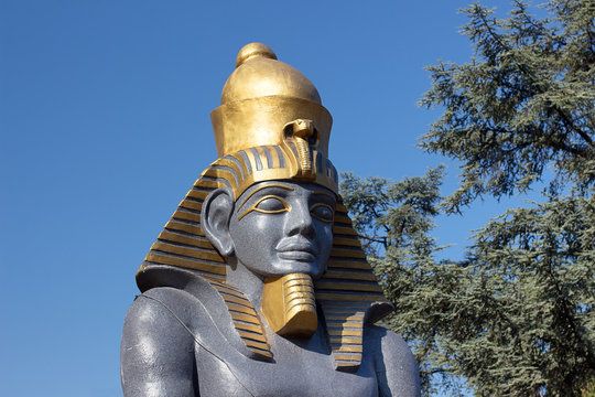 Statue of Pharaoh against a background of blue sky and trees. Decorative sculptures with Egyptian motives