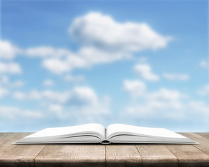 Open book is on wood planks over cloudy sky background