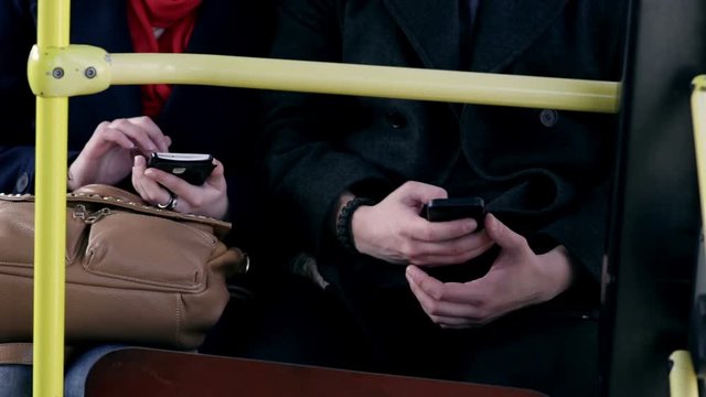 Young couple sit together on a bus and use smartphones
