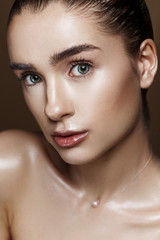 Fototapeta premium Strobing or Highlighting makeup. Closeup portrait of beautiful girl with strobing highlighter powder. Nice Glow. Perfect retouch. Studio photo beige background. Wet body effect