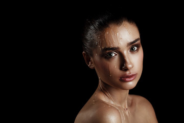 Beauty Portrait of Young Woman with Strobing Makeup Liquid on Face. Wet Body Effect. Strobing Highlighting technique. Professional Retouch. Studio Photo. Ideal commercial concept. Black background