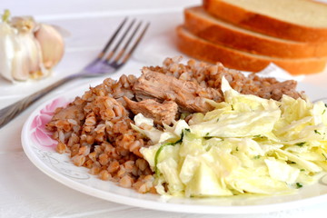 Buckwheat porridge with meat, cabbage salad, bread, garlic, fork on a white wooden background