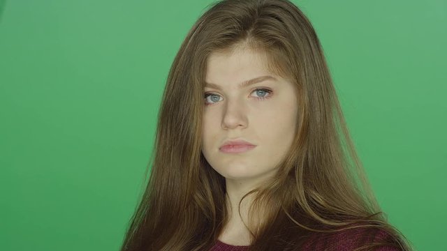 Young brunette woman runs her fingers through her hair stares blankly, on a green screen studio background