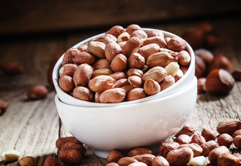 Raw peeled peanuts in a white porcelain bowl, old wooden backgro
