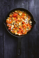 fried mushrooms with vegetables in a black frying pan on a wooden dark background. top view