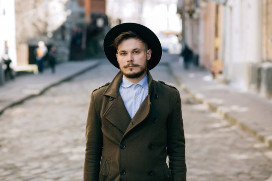 Handsome Young Bearded Hipster Man Guy In Hat Fedora On Street With Suitcase. Retro Vintage Fashion Look