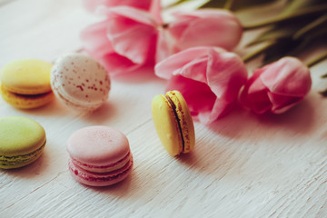 A beautiful bouquet of pink tulips with colorful macaroons on white wooden background