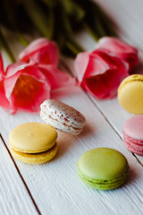 A beautiful bouquet of pink tulips with colorful macaroons on white wooden background